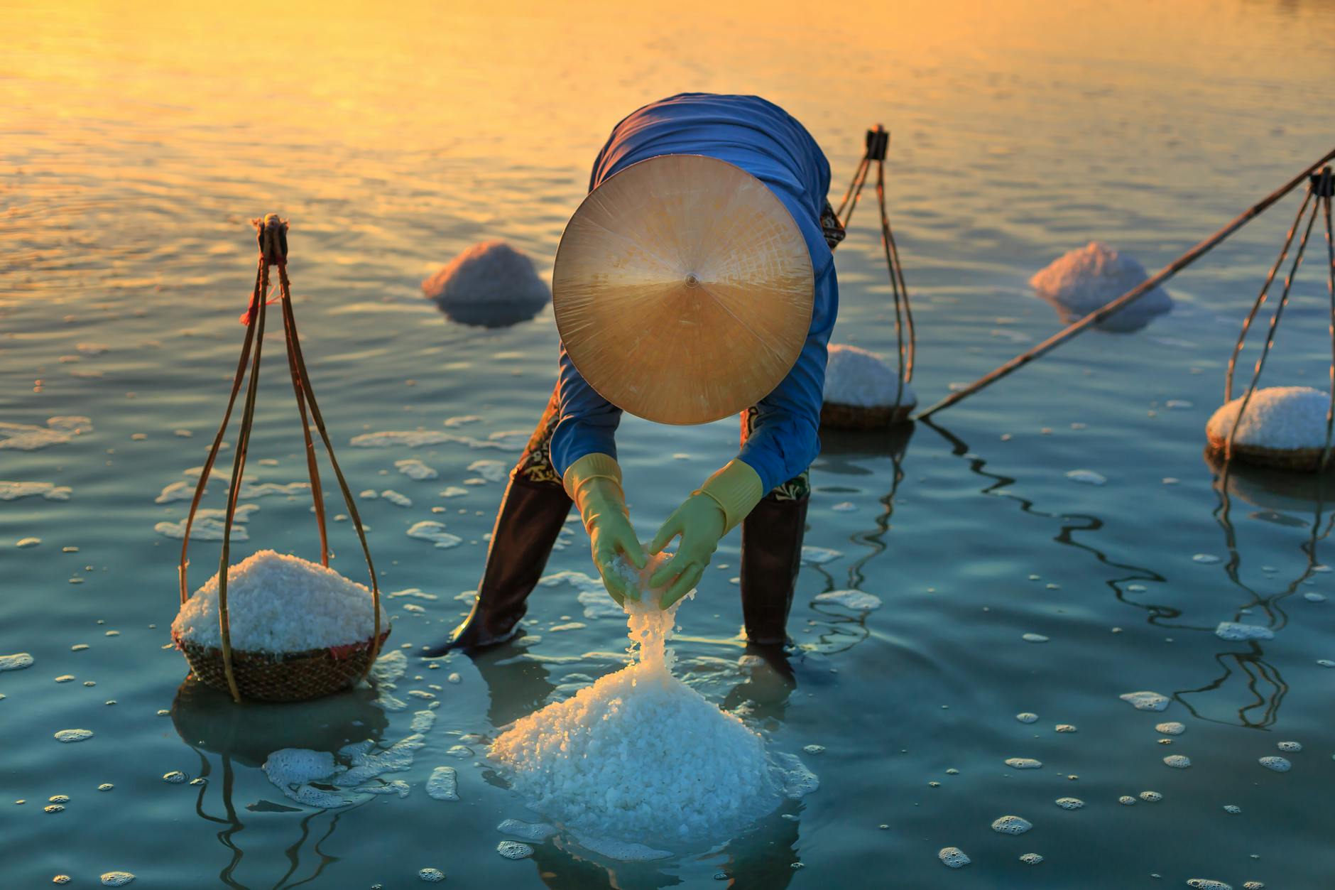 Kobieta zbierająca sól o zachodzie słońca na azjatyckim polu Kobieta zbierająca sól o zachodzie słońca na azjatyckim polu