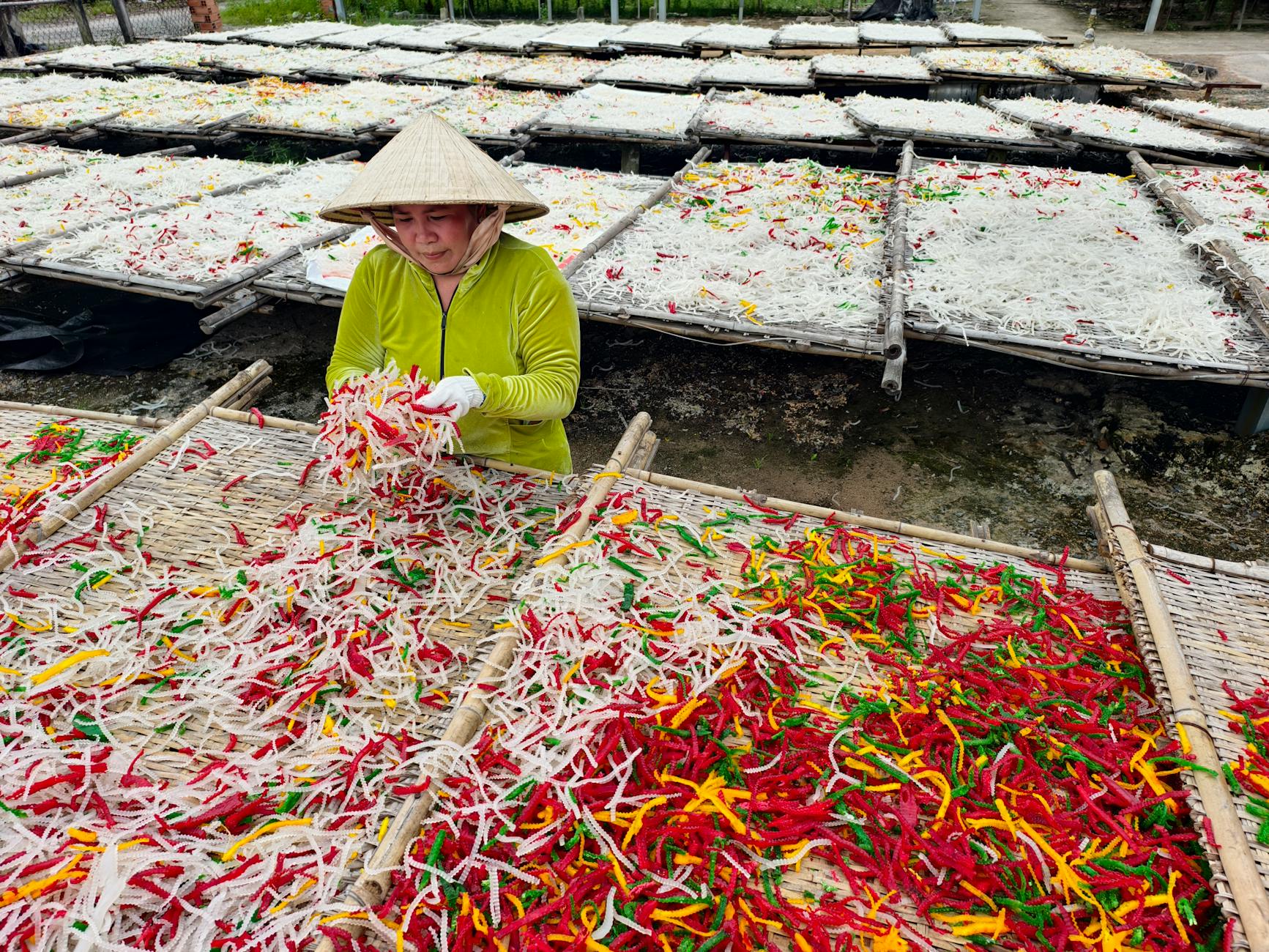 Osoba układa kolorowe suszone warzywa na bambusowych suszarkach na zewnątrz