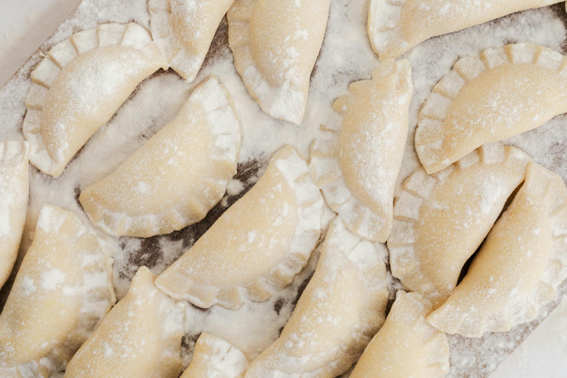 Surowe domowe pierogi na drewnianej tacy oprószonej mąką