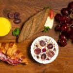 Zdrowe śniadania w podróży po Lubelskiem: lokale, które karmią lekko i smacznie Lekkie śniadanie: croissant, bagietka, winogrona, jogurt i sok na stole