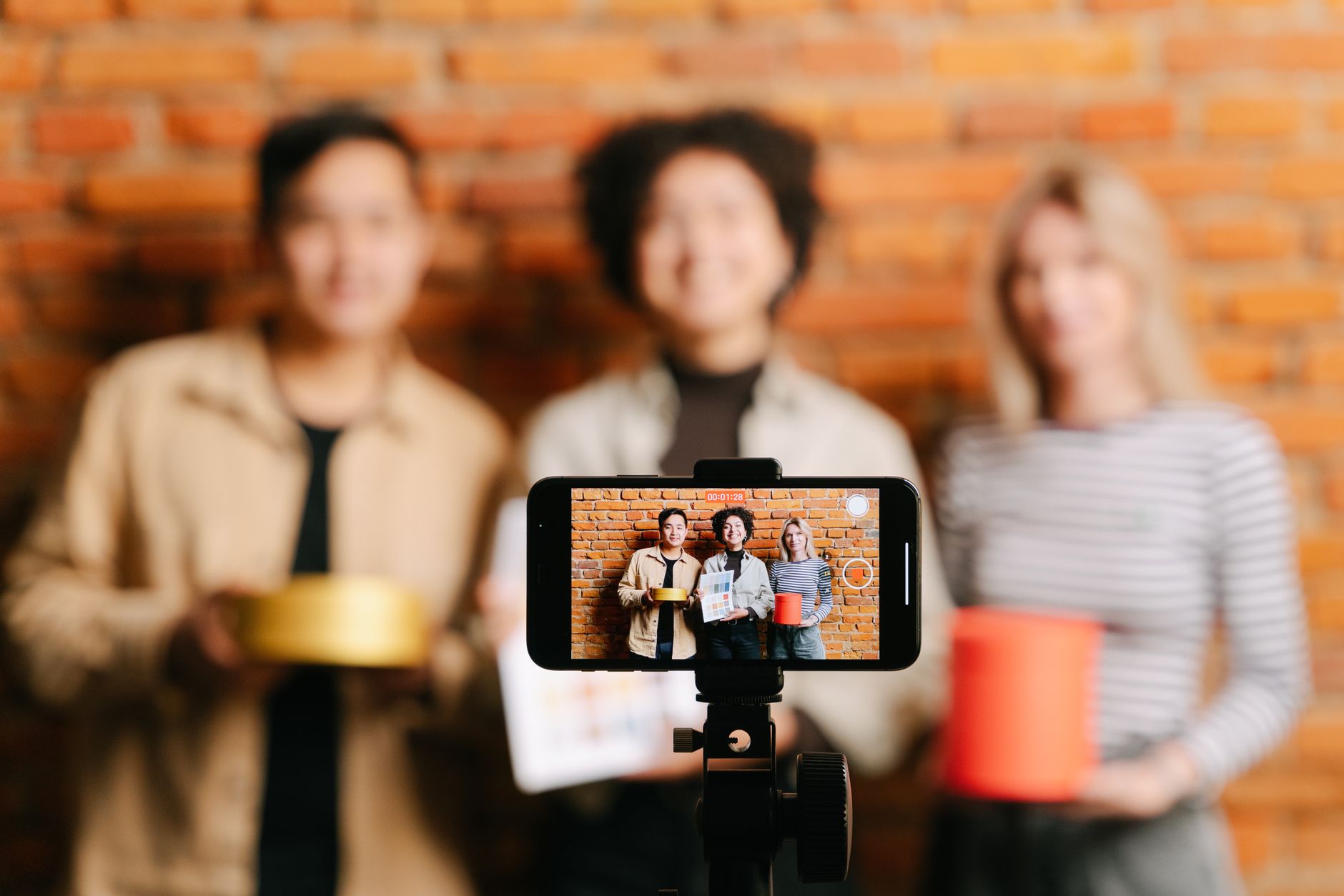 Zespół influencerów nagrywa wspólny film smartfonem na tle ceglanej ściany